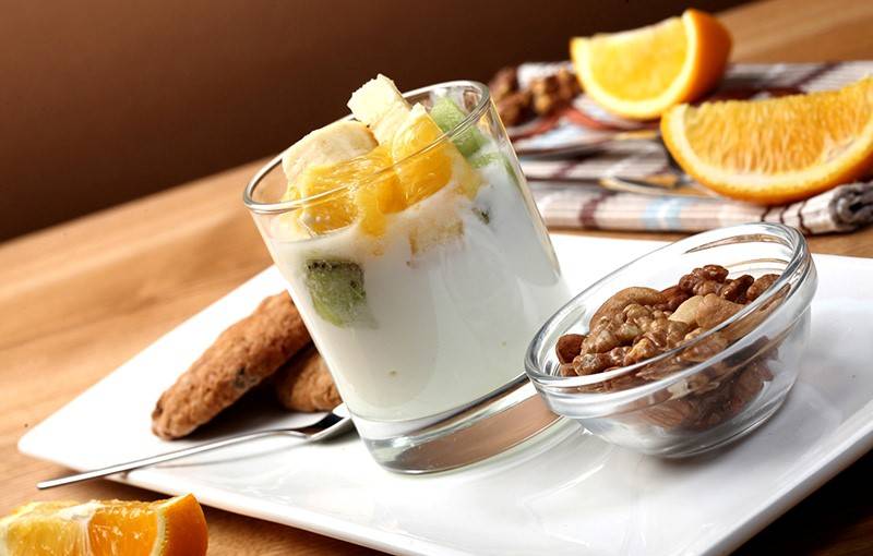 Obst in Joghurt im Glas mit Nüssen und Keksen auf Teller